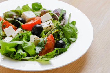 Greek salad in white plate. Fresh vegetable salad of tomatoes, olives, feta cheese, lettuce and herbs and dressed with salt, pepper and olive oil.
