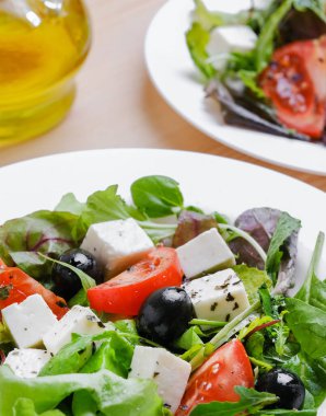 Greek salad in white plate. Fresh vegetable salad of tomatoes, olives, feta cheese, lettuce and herbs and dressed with salt, pepper and olive oil.