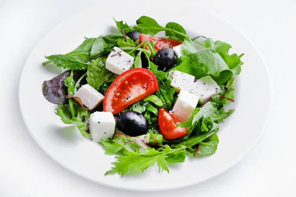 Greek salad in white plate. Fresh vegetable salad of tomatoes, olives, feta cheese, lettuce and herbs and dressed with salt, pepper and olive oil.