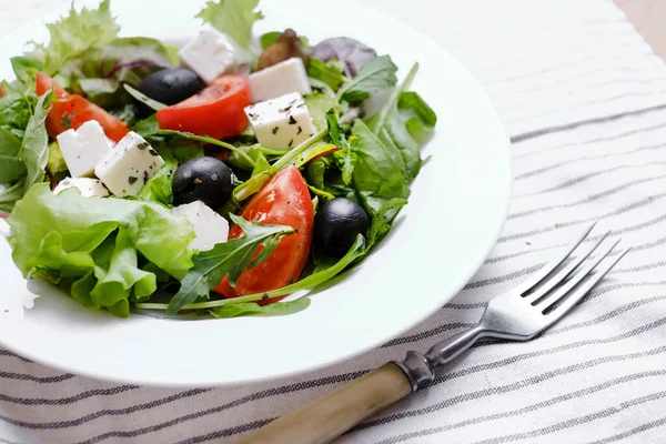 Greek salad in white plate. Fresh vegetable salad of tomatoes, olives, feta cheese, lettuce and herbs and dressed with salt, pepper and olive oil.