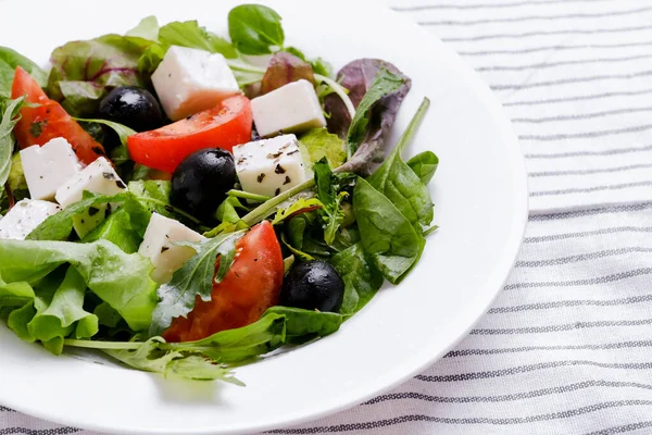 Greek salad in white plate. Fresh vegetable salad of tomatoes, olives, feta cheese, lettuce and herbs and dressed with salt, pepper and olive oil.
