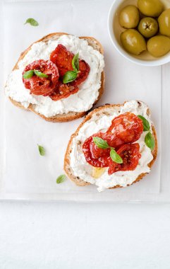 İki bruschetta peynirli, zeytinli ve kurutulmuş domatesli ciabatta ekmekli beyaz arka planda. Zeytinyağı ve baharatlar süslenmiş. Kopyalama alanı. Üst görünüm