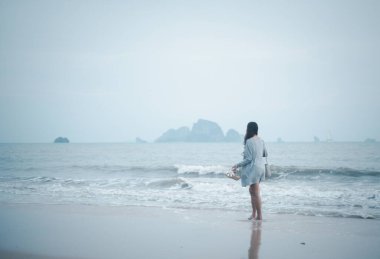 Yalnız bir kadın, deniz arka planında fırtınalı bir deniz yüzeyinde tek başına yürüyor.