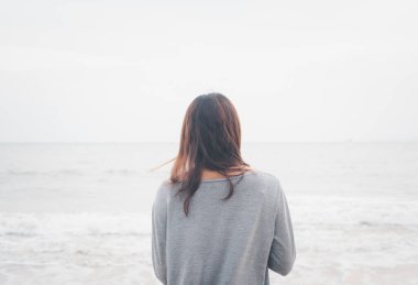 Yalnız bir kadın, deniz arka planında fırtınalı bir deniz yüzeyinde tek başına yürüyor.