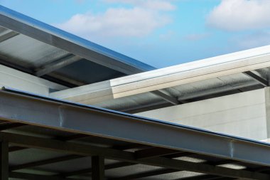 Ahşap görünümlü metal levha beyaz süslemeli çatı geçidi, korbel, beyaz yatay kaplamalı hoparlör mavi gökyüzü arka planlı lüks bir eve.