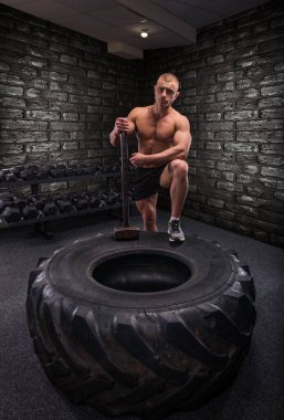 Çekiçle vücut geliştirici ve spor salonunda büyük bir tekerlek.