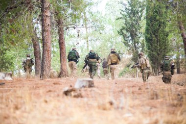 Bir grup asker ormanda koşuyor. Airsoft takım oyunu. Askeri üniformalı oyuncular takımı.