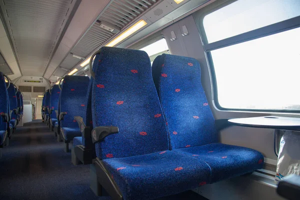Empty train car with seats. Empty train seats with a passage to the inside of the car. Near the seats there is a window and a table. Travel alone. The seats in the carriage are blue and there are no people at all.