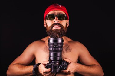 The guy on a black background with a smile. Photographer in a cap with a large camera and lens. creative torment