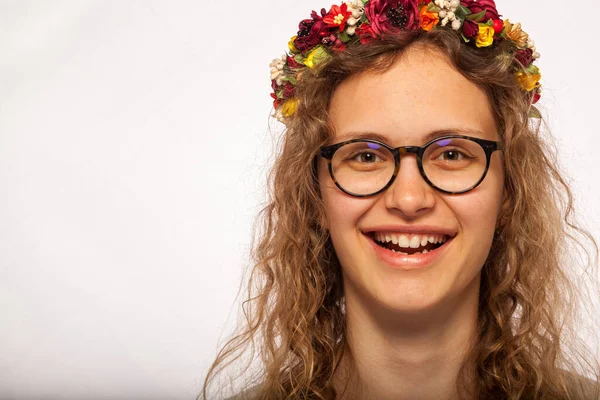 A young and beautiful model is smiling. A wreath of flowers is worn on the head. Pleasant and beautiful smile of a girl in glasses. Sincere emotions of joy in a young girl with curly mustache.