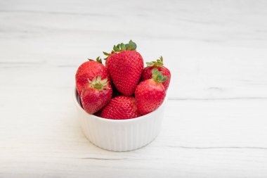 Taze olgun lezzetli çilekler, gri bir arka planda beyaz bir kasede..