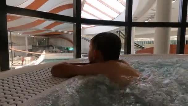 Chłopiec w jacuzzi z tyłu jacuzzi. rodzinne wakacje w parku wodnym — Wideo stockowe