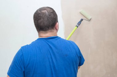 Paten boyama duvarı olan bir adam. Boya silindirini kapat. Aileyle birlikte ev onarımı. Güncelleme, iyileştirme salonu.