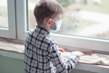 Koronavirüs salgını sırasında karantina altındaki çocuk evde oturur ve pencereden dışarı bakar..