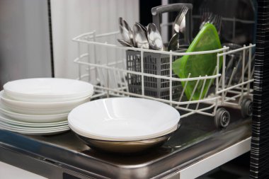 Open dishwasher with white clean dishes after washing in kitchen