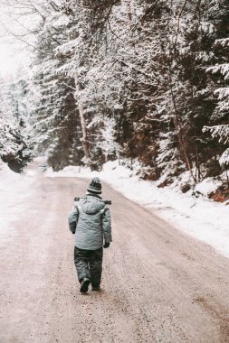 Küçük bir erkek ceketi karlı bir ormanda yürüyor. Bir kış günü temiz havada yürümek. Yaşam tarzı kavramı.