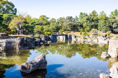 Sığ bir gölet ve gün ışığında etrafı kayalarla çevrili Japon Bahçesi..