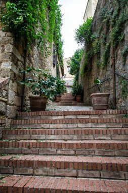Looking up a series of old, weathered brick stairs between the stone houses in the Italian village of San Gimignano in Tuscany, Italy, Europe.