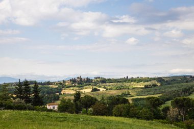 Rural view of Tuscany with rolling green hills and traditional Tuscan architecture on a partly sunny day.