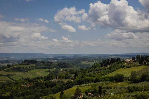 Rural view of Tuscany with rolling green hills and traditional Tuscan architecture on a partly sunny day.
