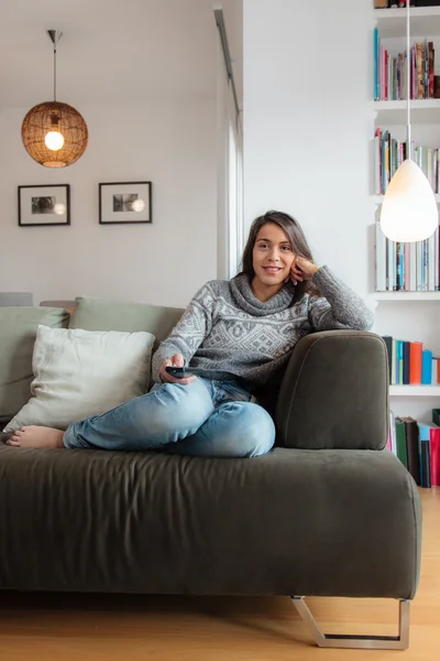 Молодая женщина смотрит телевизор дома на диване — стоковое фото