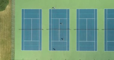 Dört tenisçi yaz aylarında bir park bölgesi tenis kortunda birbirlerine karşı gösteri yapıyorlar..