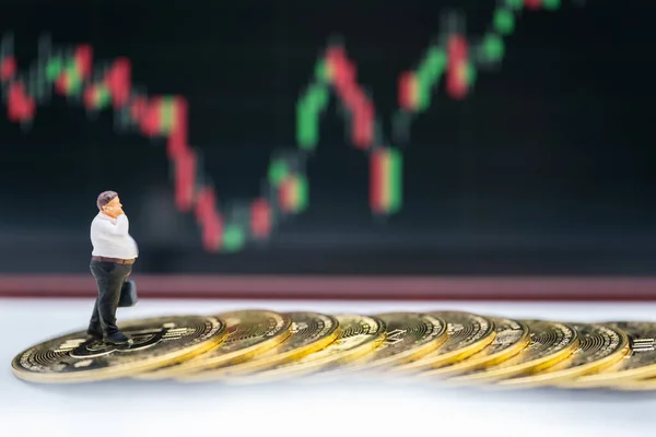 Business Money and Financial Concept. Fat businessman miniature figure people make a phone call and holding hand bag walking on pile of gold Bitcoin coins with candlestick chart as background.