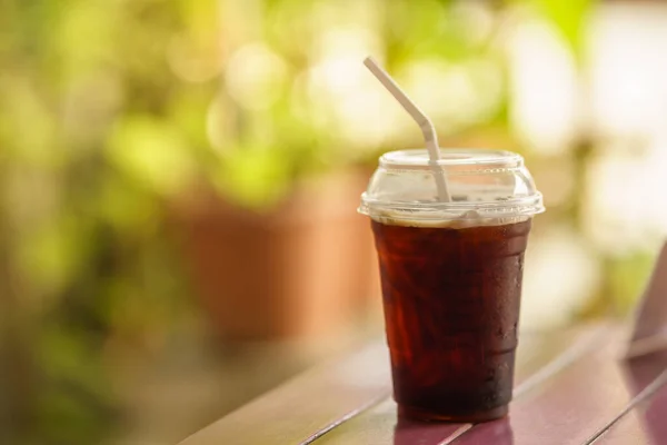 Yakın plan plastik fincan buzlu kahve Americano. Tahta masa üzerinde yeşil doğa arka planlı..