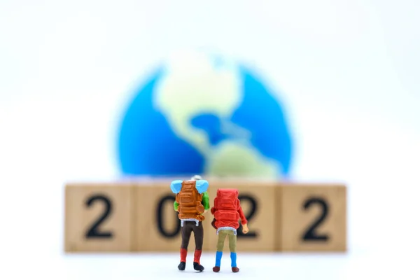 2022年新年及旅游概念 两个带背包的旅行家缩影 背负着一堆木制的数字块和白色背景的迷你世界球 — 图库照片