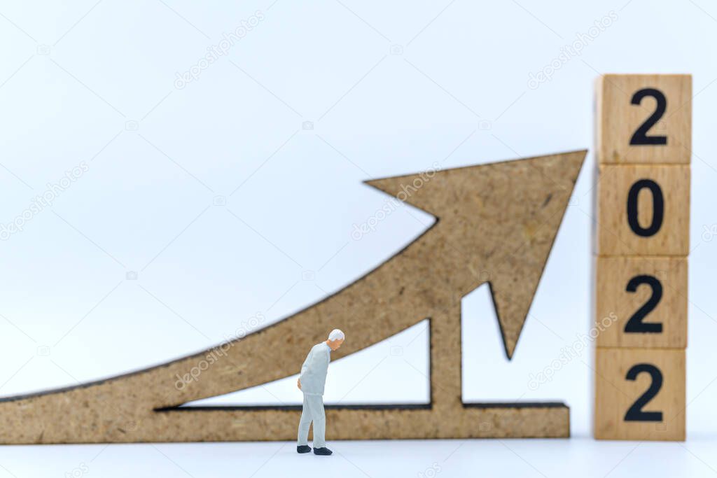 2022 New Year and Business Planning Concept. Closeup of businessman miniature figures waling with arrow sign with wooden number block on white background.