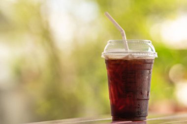 Yakın plan plastik fincan buzlu kahve Americano. Tahta masa üzerinde yeşil doğa arka planlı..