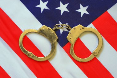 Kelepçeler ve Amerikan Bayrağı. ABD hukuk sistemi kavramı, Amerikan bayrağı arka planda kelepçe