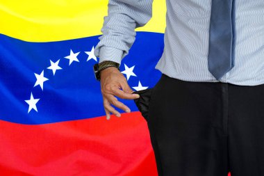Takım elbiseli bir adam pantolonunun cebini ters yüz ediyor ve arka planda Venezuela bayrağının boş olduğunu gösteriyor. Kriz, işsizlik, Venezuela 'da iflas kavramı