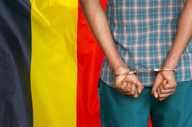 African man with handcuffs on the background of the Belgium flag. Back view. Concept of prisons and corruption in Belgium