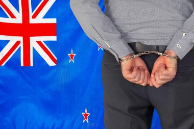 Male with handcuffs on the background of the New Zealand flag. Back view. Concept of prisons and corruption in New Zealand