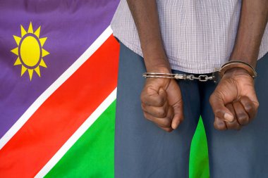 African man with handcuffs on the background of the Namibia flag. Back view. Concept of prisons and corruption in Namibia