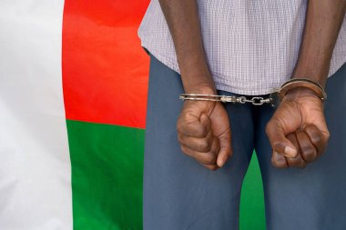 African man with handcuffs on the background of the Madagascar flag. Back view. Concept of prisons and corruption in Madagascar