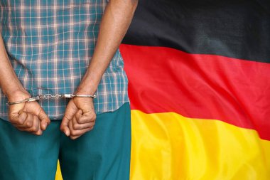 African man with handcuffs on the background of the Germany flag. Back view. Concept of prisons and corruption in Germany