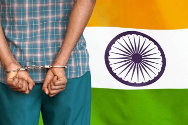 African man with handcuffs on the background of the India flag. Back view. Concept of prisons and corruption in India