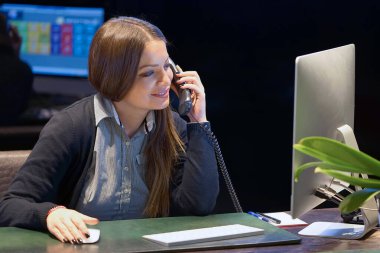 Ofiste çalışan genç bir kadın telefonda konuşuyor. Otel yöneticisi.