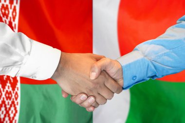 İki bayrağın arka planında iş tokalaşması. Beyaz Rusya ve Madagaskar bayrağının arka planında el sıkışan erkekler. Destek konsepti