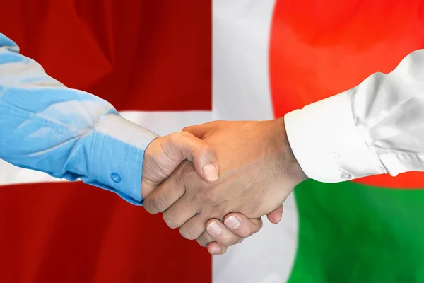 2つのフラグを背景にビジネス握手 マダガスカルとラトビアの国旗を背景に男性が握手をする サポートコンセプト — ストック写真
