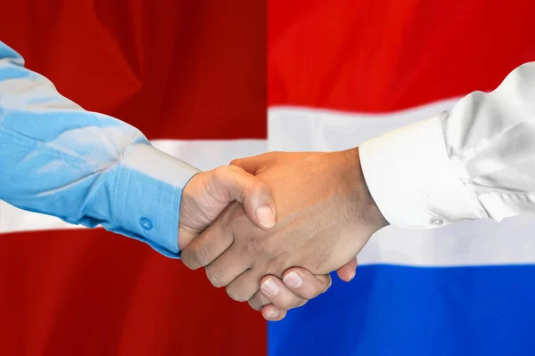 2つのフラグを背景にビジネス握手 オランダやラトビアの国旗を背景に握手をする男性 サポートコンセプト — ストック写真