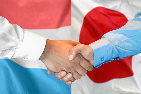 Деловое рукопожатие на фоне двух флагов. Мужчины пожимают руки на фоне флага Люксембурга и Японии. Концепция поддержки