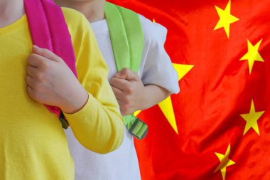 Çin bayrağının arka planında çantaları olan iki çocuk. Çin 'de çocuk yetiştirme ve eğitme kavramı