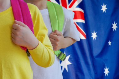Avustralya bayrağının arka planında çantaları olan iki çocuk. Avustralya 'da çocuk yetiştirme ve eğitme kavramı