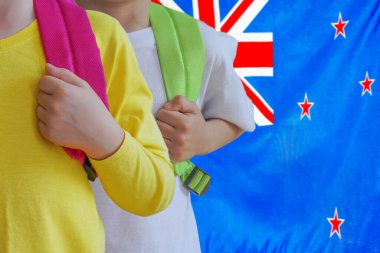 Yeni Zelanda bayrağına sahip çantalı iki çocuk. Yeni Zelanda 'da çocuk yetiştirme ve eğitme kavramı