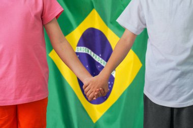 Brezilya bayrağında el ele tutuşan iki çocuk. Erkek ve kız Brezilya 'nın arka plan bayrağında el ele verdiler. Brezilya 'da aile ve ebeveynlik kavramı