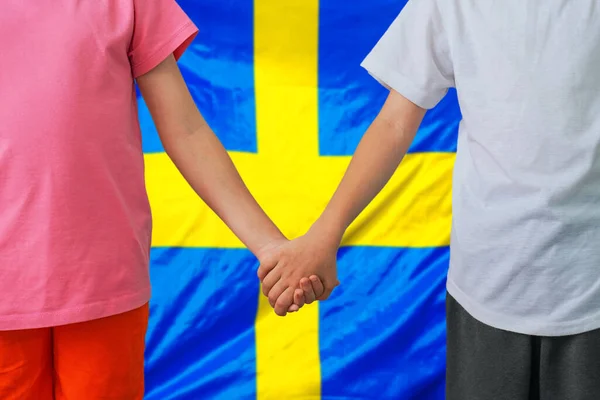 两个孩子手拉手在瑞典国旗的背景上 男孩和女孩手拉手在瑞典的背景旗上 瑞典家庭和养育子女的概念 — 图库照片