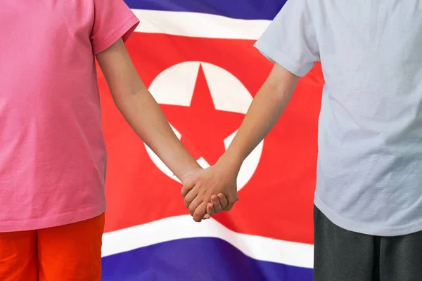 Two children joined hands on flag North Korea background. Boy and girl joined hands on background flag of North Korea. Concept of family and parenting in North Korea